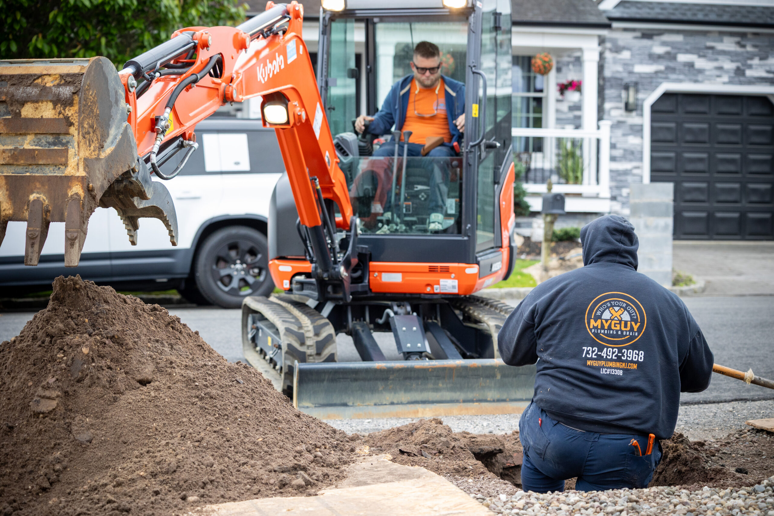 man working in ground hole and backhoe